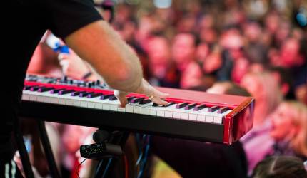Artist play on audio piano on stage in a concert hall behing peoples.